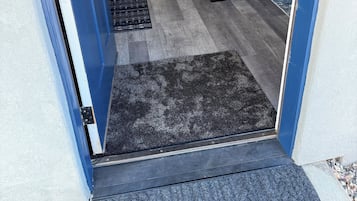 A doorway leading to a living area with a grey sofa, a black rug, and a clock on the wall.