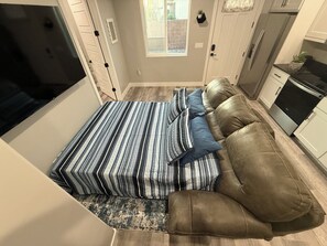 Un espacio habitable funcional con sofá cama, kitchenette y ventana que ofrece luz natural.