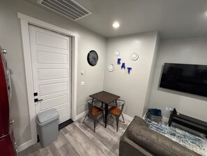 Un espacio habitable pequeño con una mesa de comedor, un sofá, un televisor y una puerta.