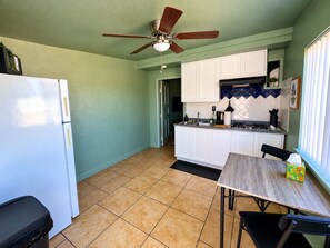 A kitchen with white cabinets, a wooden table, a ceiling fan, and a window with blinds. - The Fremont Studio - 2min from Fremont St! (Las Vegas)