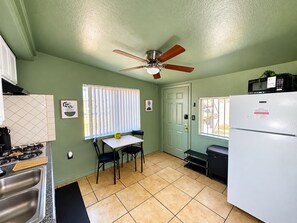 A kitchen with a ceiling fan, a refrigerator, a dining table with chairs, and a window with blinds. - The Fremont Studio - 2min from Fremont St! (Las Vegas)