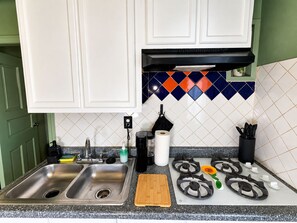 A kitchen with a double sink, a wooden cutting board, a gas stove, and a colorful backsplash. - The Fremont Studio - 2min from Fremont St! (Las Vegas)