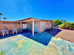 A residential property with a covered patio, two white plastic chairs, a small table, and a potted plant. - The Fremont Studio - 2min from Fremont St! (Las Vegas)