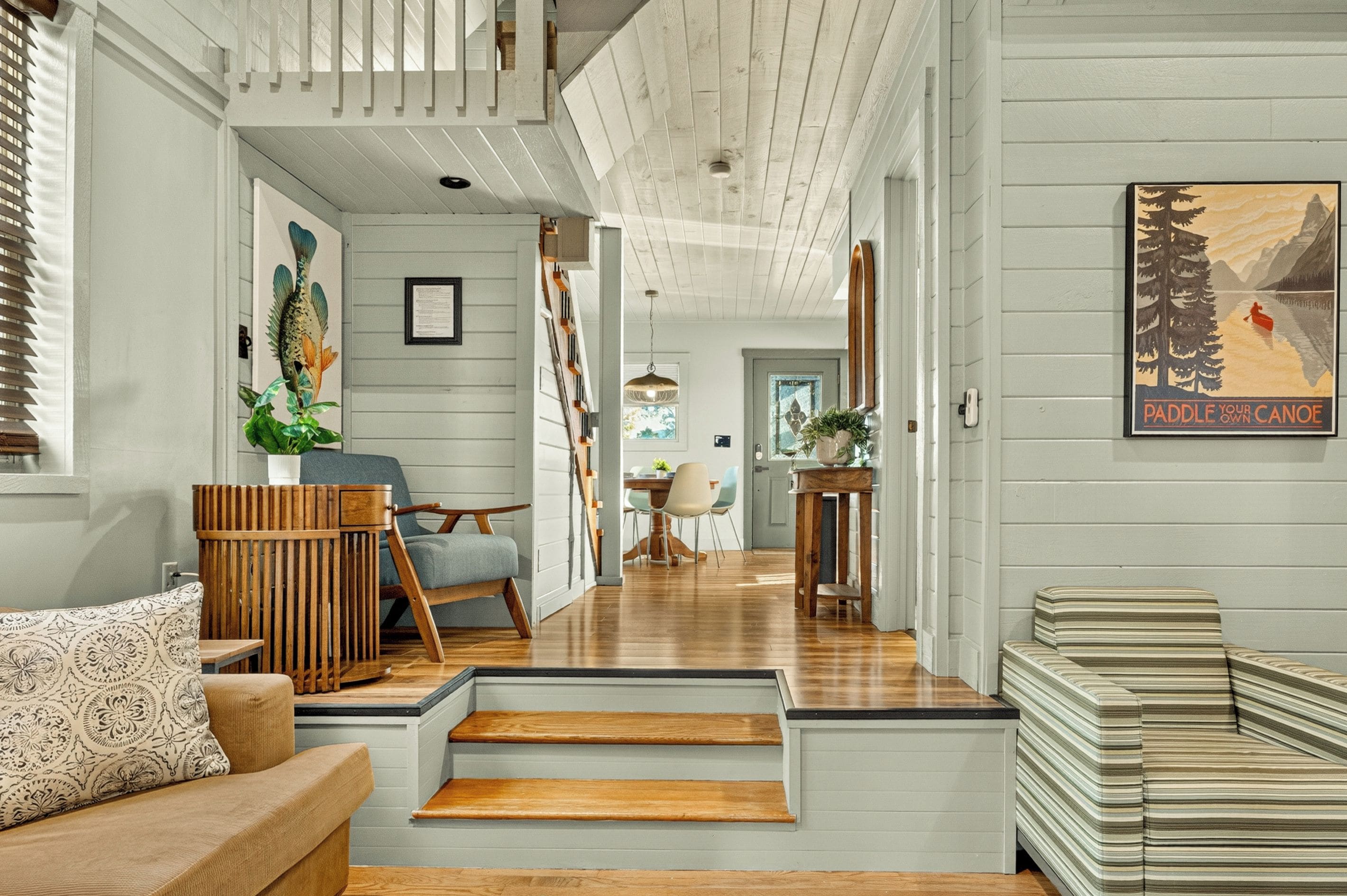 A modern interior with a staircase leading to a dining area, wooden flooring, and a view of a mountain landscape.