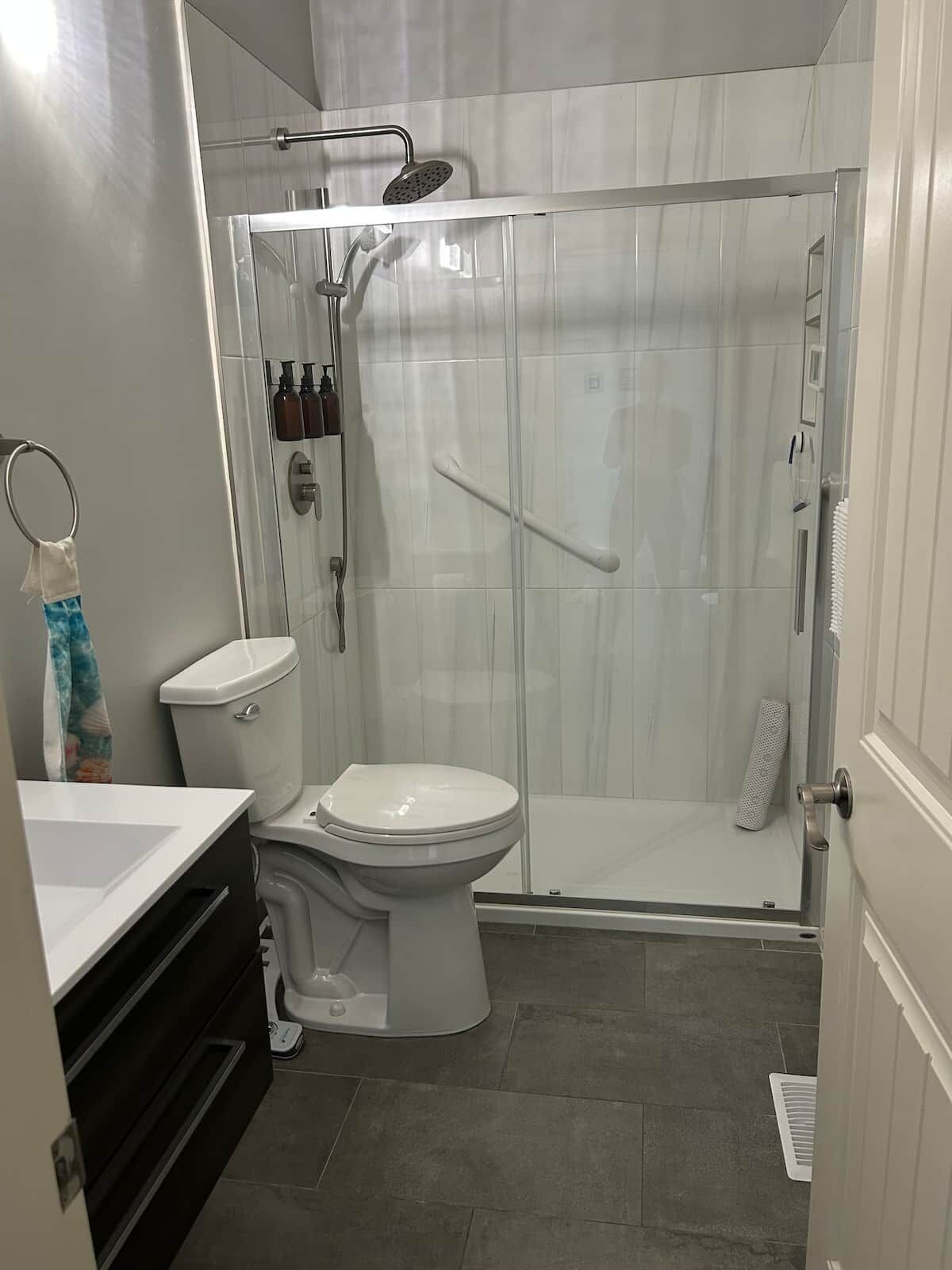 A bathroom with a glass-enclosed shower, a white toilet, and a sink with a towel rack.