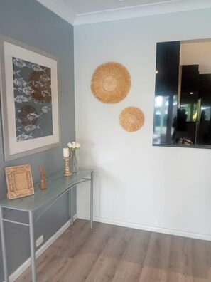 Een kamer met een grijze muur, een lijst met een abstract schilderij, een glazen console tafel met decoratieve objecten, en twee geweven wanddecoraties.