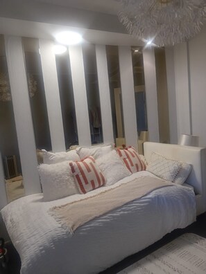 Een slaapkamer met een bed, kussens, een nachtkastje en een spiegel.