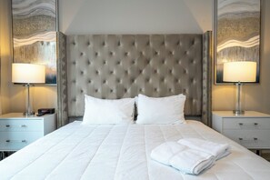 A hotel room with a tufted headboard, two white pillows, a neatly made bed, a bedside table with a lamp, and a wall-mounted mirror. - 5BR Condo with Rooftop & Game Room Near Disney (Kissimmee)