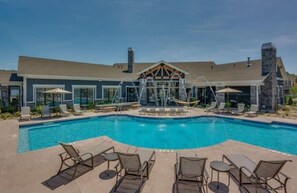A swimming pool with lounge chairs and umbrellas, a covered area with a stone facade, and a clear sky. - 5BR Condo with Rooftop & Game Room Near Disney (Kissimmee)