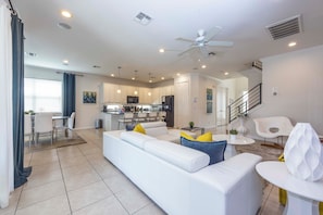A modern living room with a white sofa, a dining area with a table and chairs, a kitchen with white cabinets, and a staircase leading to another level. - Prime Location Near Parks at Bella Vida Resort (Kissimmee)