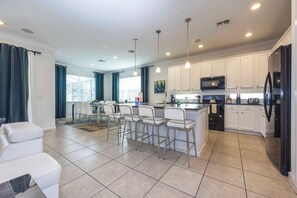 A modern kitchen with white cabinets, a black refrigerator, and a bar area with white stools. - Prime Location Near Parks at Bella Vida Resort (Kissimmee)
