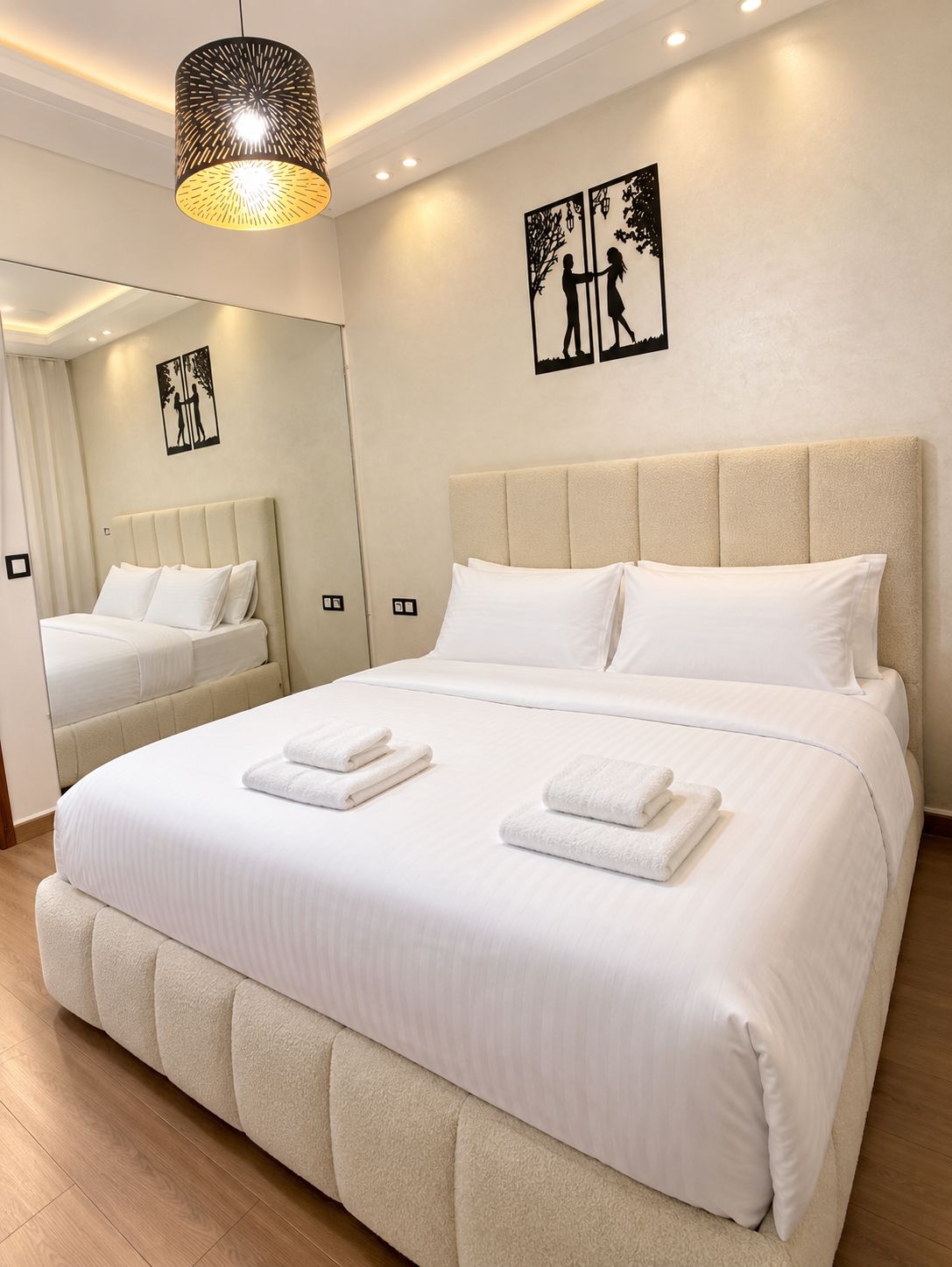 A hotel room with a large bed, a headboard, a mirror, and artwork on the wall.