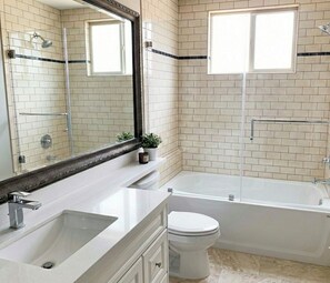 A bathroom with a bathtub, toilet, sink, and a large mirror. - Luxury Richmond Home (Richmond)