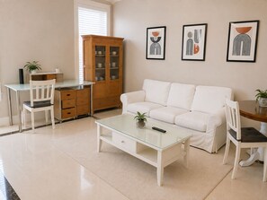 A living room with a white sofa, a glass coffee table, a wooden cabinet, and three framed abstract artworks on the wall. - Luxury Richmond Home (Richmond)
