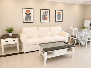 A living room with a white sofa, a glass coffee table, a side table with a plant, and framed abstract art on the wall. - Luxury Richmond Home (Richmond)