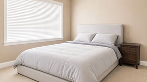 A bedroom with a bed, nightstand, and window with blinds. - Luxury Richmond Home (Richmond)