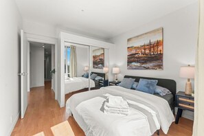 A hotel room with a large bed, bedside tables, a mirror, and artwork on the wall. - Cozy & Chic Downtown Oasis (Vancouver)