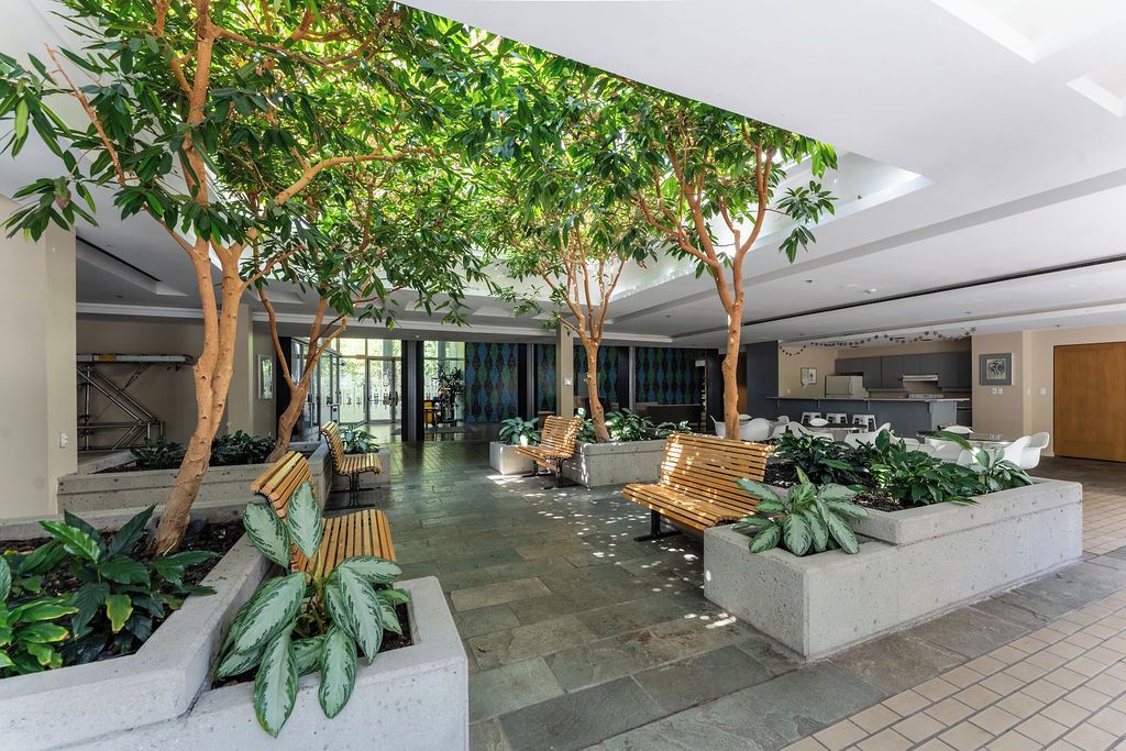 An indoor atrium with a central seating area, surrounded by planters and trees. - Cozy & Chic Downtown Oasis (Vancouver)