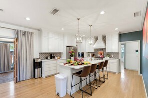 A modern kitchen with white cabinetry, a central island, bar stools, and a dining table set for a meal.