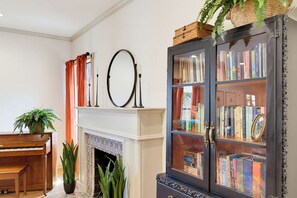 Ein Wohnzimmer mit Kamin, Klavier, Bücherregal und Spiegel.