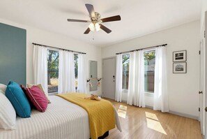Ein Schlafzimmer mit einem Bett, einem Deckenventilator und großen Fenstern mit Vorhängen.