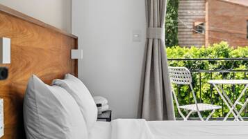 Ein Hotelzimmer mit einem Bett, einem Nachttisch, einem Holz-Kopfteil, einem Fenster mit Vorhängen und Blick auf Grünfläche.