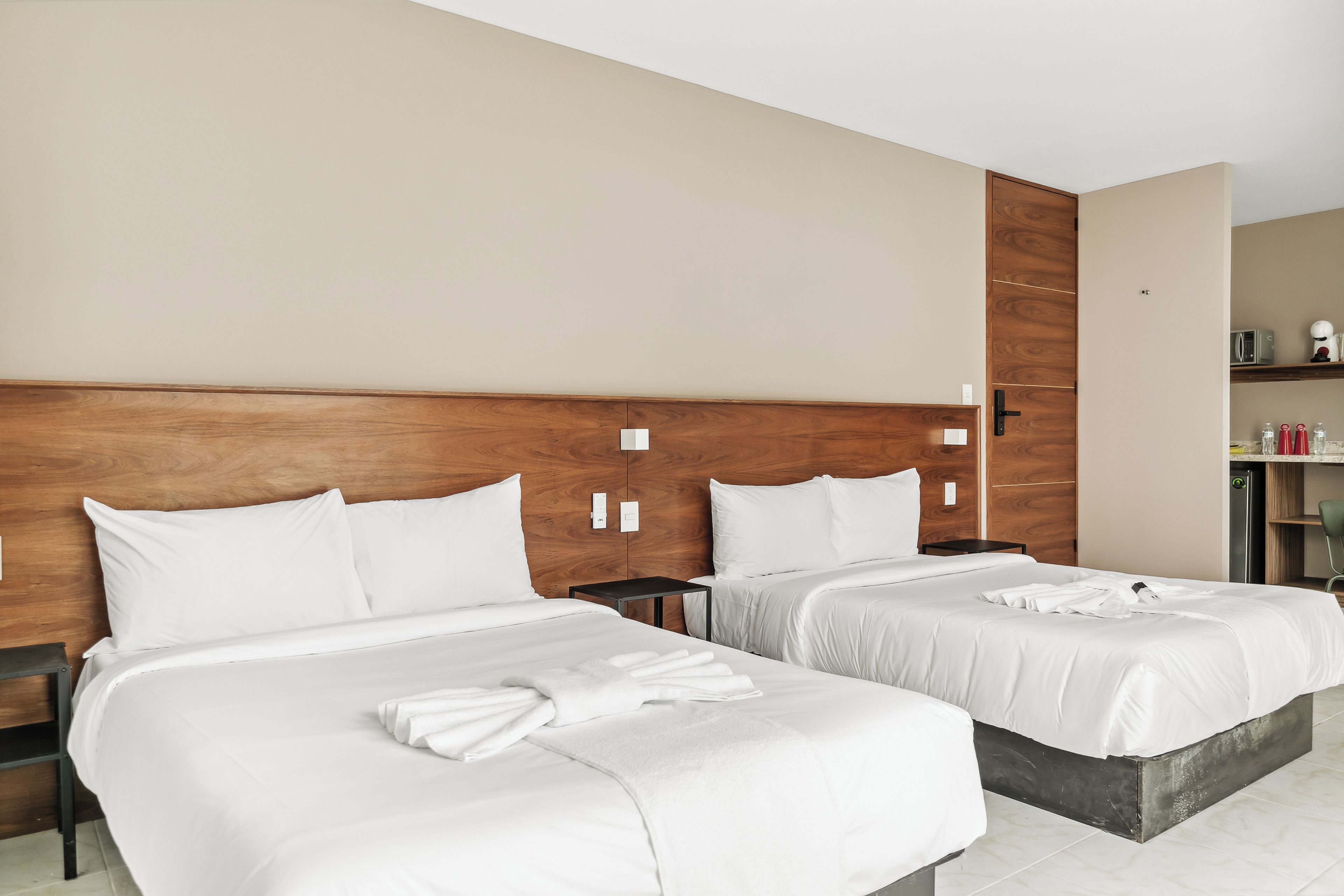 Ein Hotelzimmer mit zwei Betten, einem Holzkopfende, einem kleinen Tisch und einer Küchenzeile.
