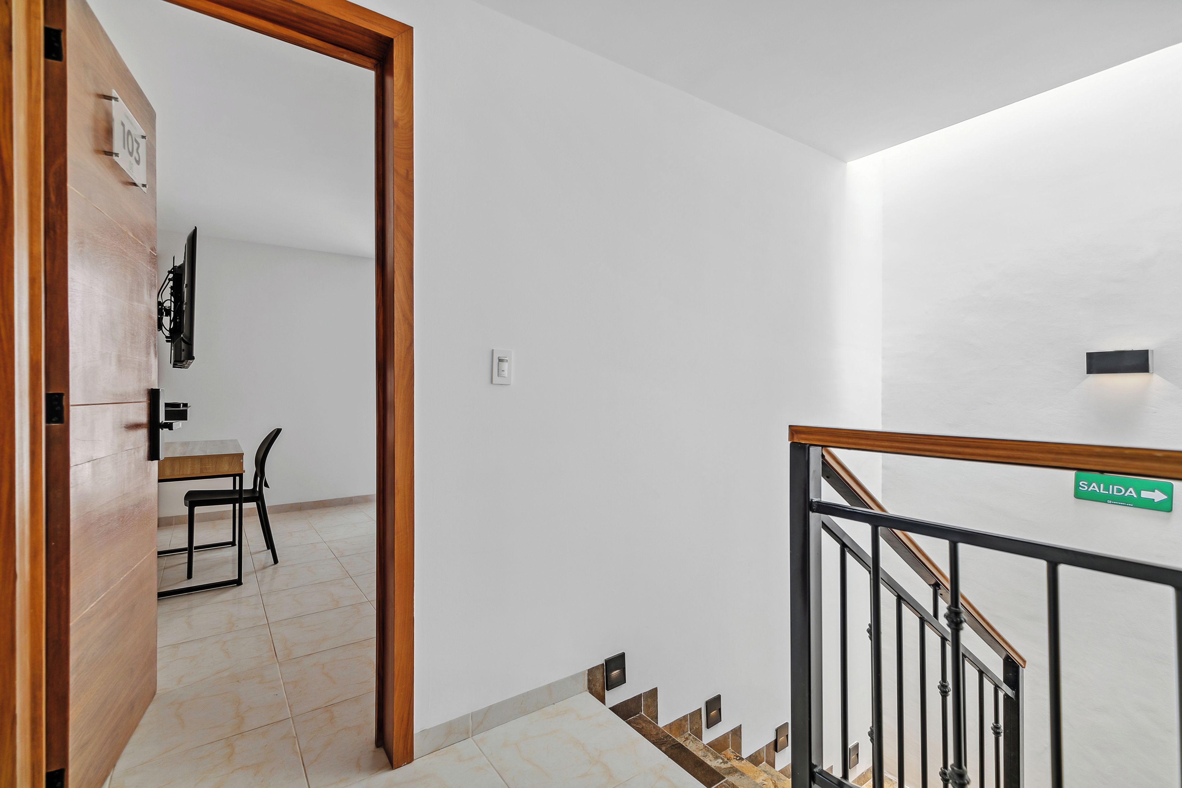 Un interior moderno con una puerta de madera, una escalera con barandilla de metal y un letrero que indica la salida.