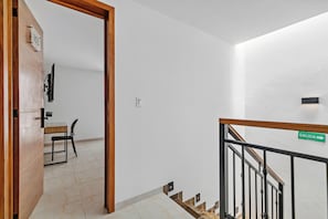 Interior moderno com porta de madeira, escada com corrimão de metal e placa indicando a saída.