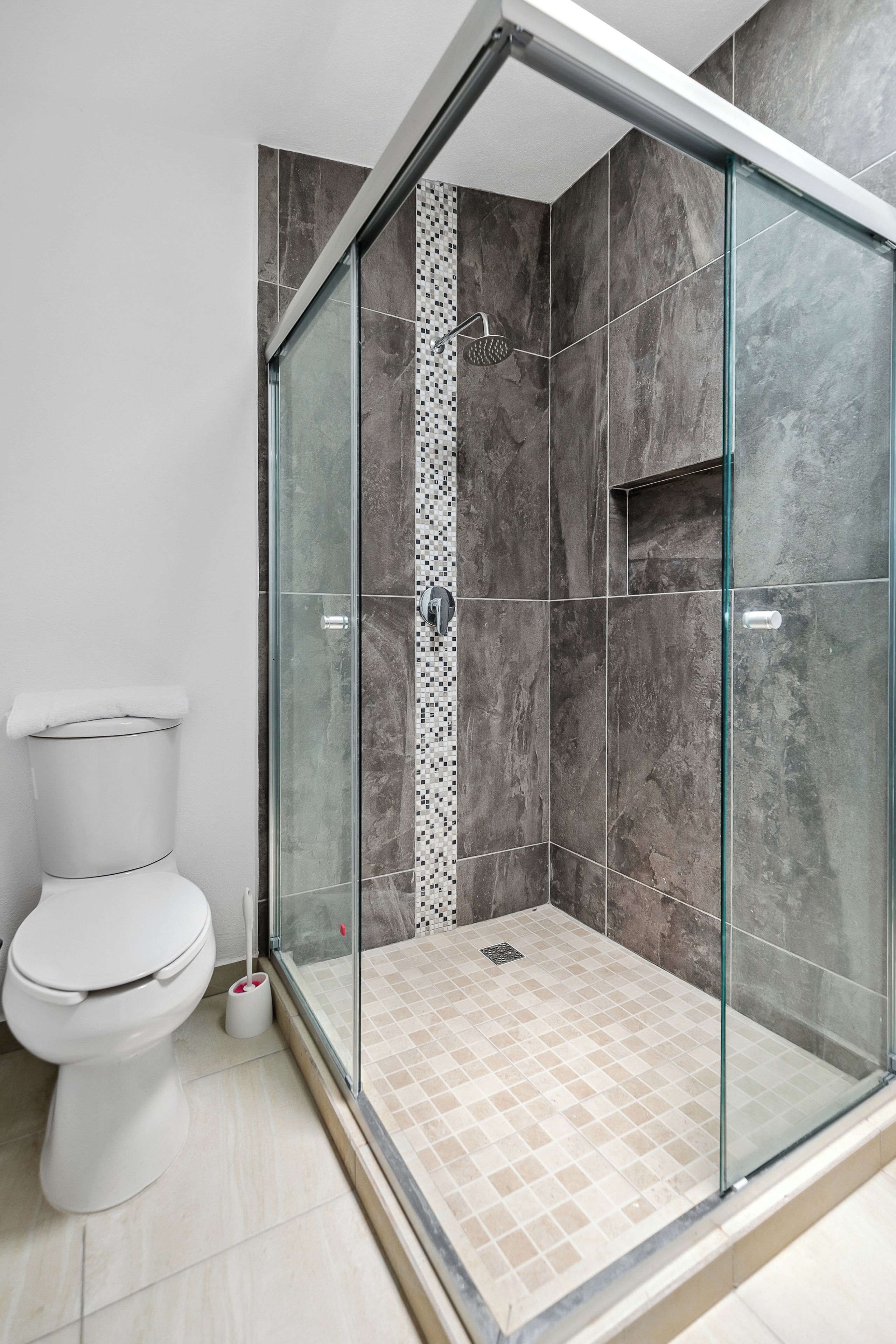 A modern bathroom with a glass-enclosed shower, a toilet, and tiled flooring.
