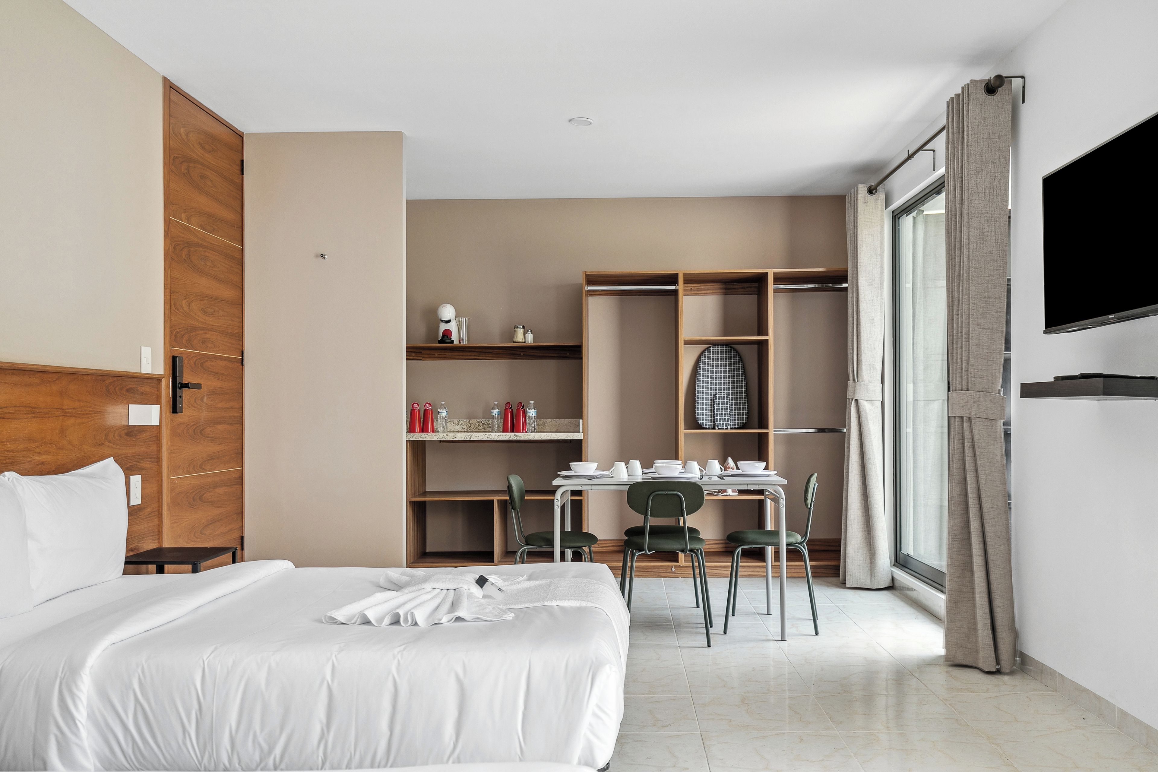 Habitación de hotel con cama, escritorio con sillas, armario y televisión.