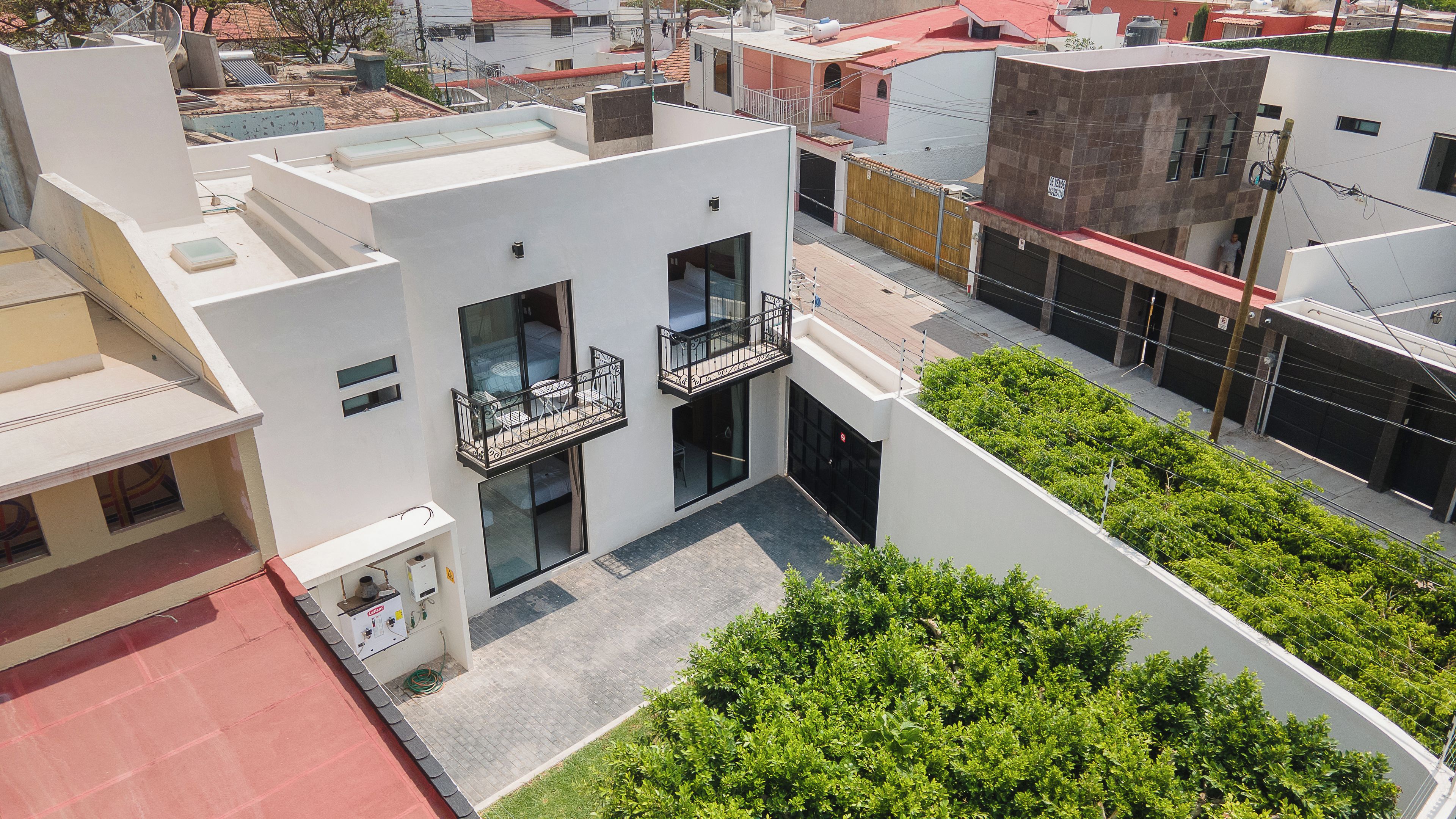 Un edificio moderno con techo plano, dos balcones con barandas de metal y una pequeña área ajardinada.