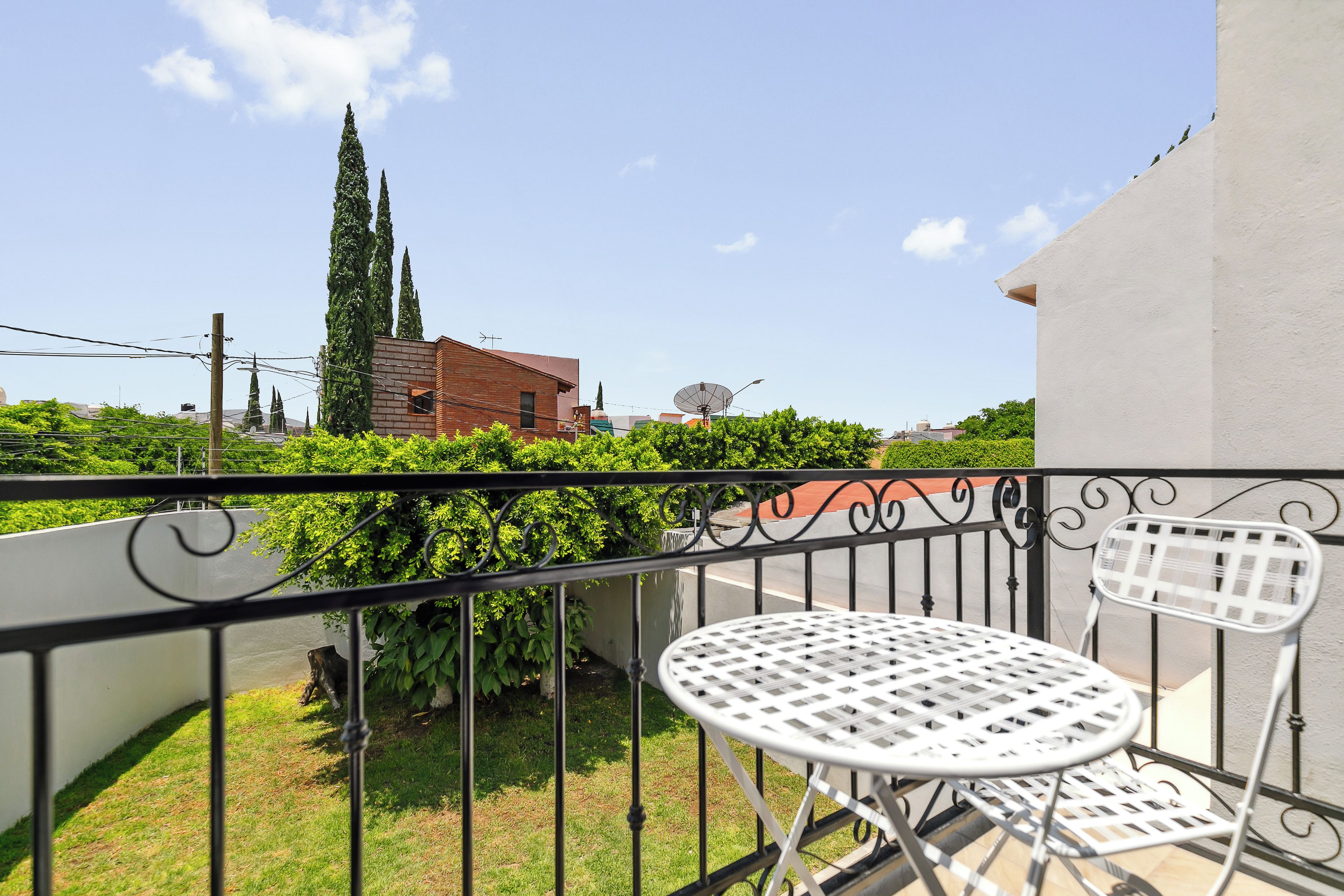 A balcony with a white metal table and chair, a view of a brick building, and a clear sky.