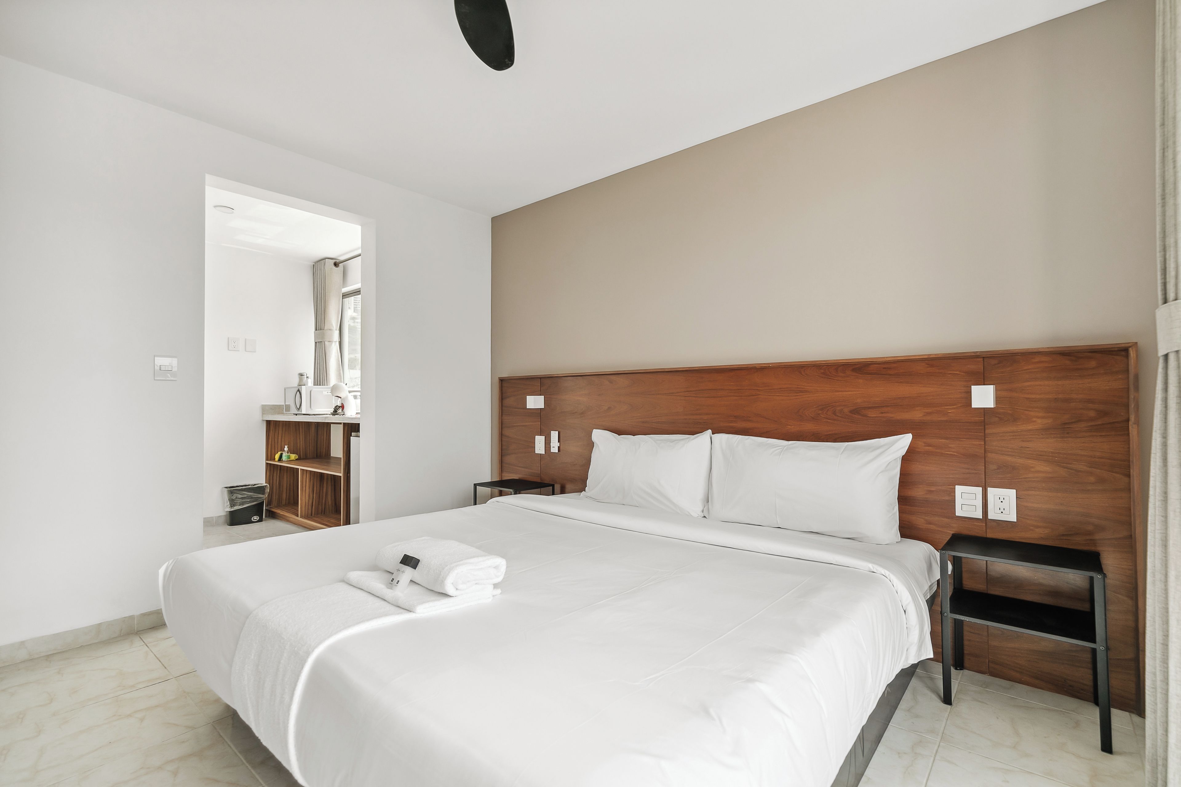 Une chambre d’hôtel avec un grand lit, une tête de lit en bois, une table de chevet et une salle de bain visible à travers une porte ouverte.