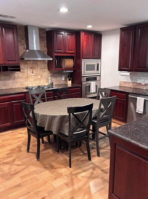 A kitchen with dark wooden cabinets, a gas stove, a microwave, and a stainless steel oven. - Charming Sanger Home - King Bed & Loft - Sleeps 6 (Sanger)