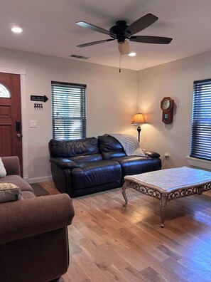 A living room with a ceiling fan, a clock, and a couch. - Charming Sanger Home - King Bed & Loft - Sleeps 6 (Sanger)