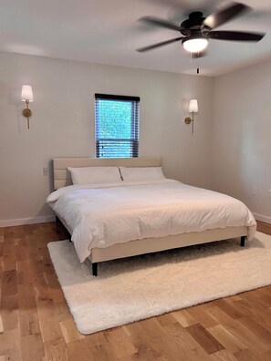 A bedroom with a bed, a ceiling fan, two wall-mounted lamps, a window with blinds, and a white rug. - Charming Sanger Home - King Bed & Loft - Sleeps 6 (Sanger)