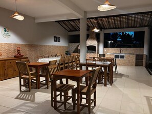 Un área de comedor al aire libre con paredes de ladrillo, mesas y sillas de madera, y luces colgantes.