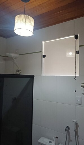 Un baño con ducha, inodoro, espejo y lámpara colgante.