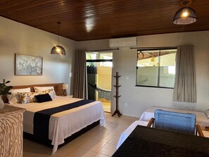 Habitación de hotel con cama, escritorio, silla, perchero y un amplio ventanal.