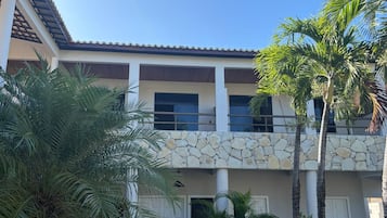 A multi-story building with a stone facade, balconies, and palm trees.
