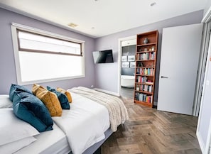 Un dormitorio con una cama, una estantería y un baño visible a través de una puerta abierta.