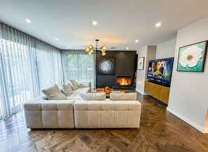A modern living room with a sectional sofa, a fireplace, and a television. - Luxury 4 Bedroom House - Sauna, 3 En-suites (Bentleigh East)