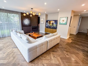 A modern living room with a sectional sofa, a coffee table, a fireplace, a TV, and artwork on the walls. - Luxury 4 Bedroom House - Sauna, 3 En-suites (Bentleigh East)