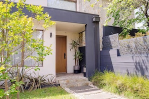 Una casa moderna amb una porta de fusta, un camí de pedra i molta vegetació.