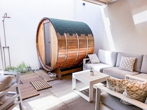 Un interior moderno con una sauna de barril de madera, un conjunto de sofás y una mesa de centro.