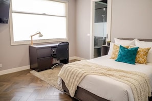 A bedroom with a bed, a desk, a chair, a window, and a shower area. - Luxury 4 Bedroom House - Sauna, 3 En-suites (Bentleigh East)
