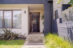 Una casa moderna con un camino de piedra que lleva a la entrada, un ventanal grande y un muro decorativo.