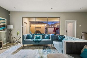 Ein modernes Wohnzimmer mit einer Eckcouch, einer Glastür, die auf einen Balkon führt, und Blick ins Freie.
