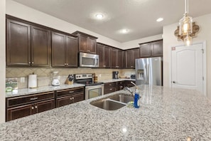 A kitchen with dark wooden cabinets, stainless steel appliances, granite countertops, and a built-in sink. - South Pool | Arcade Game Room | Near Disney 9039 (Kissimmee)